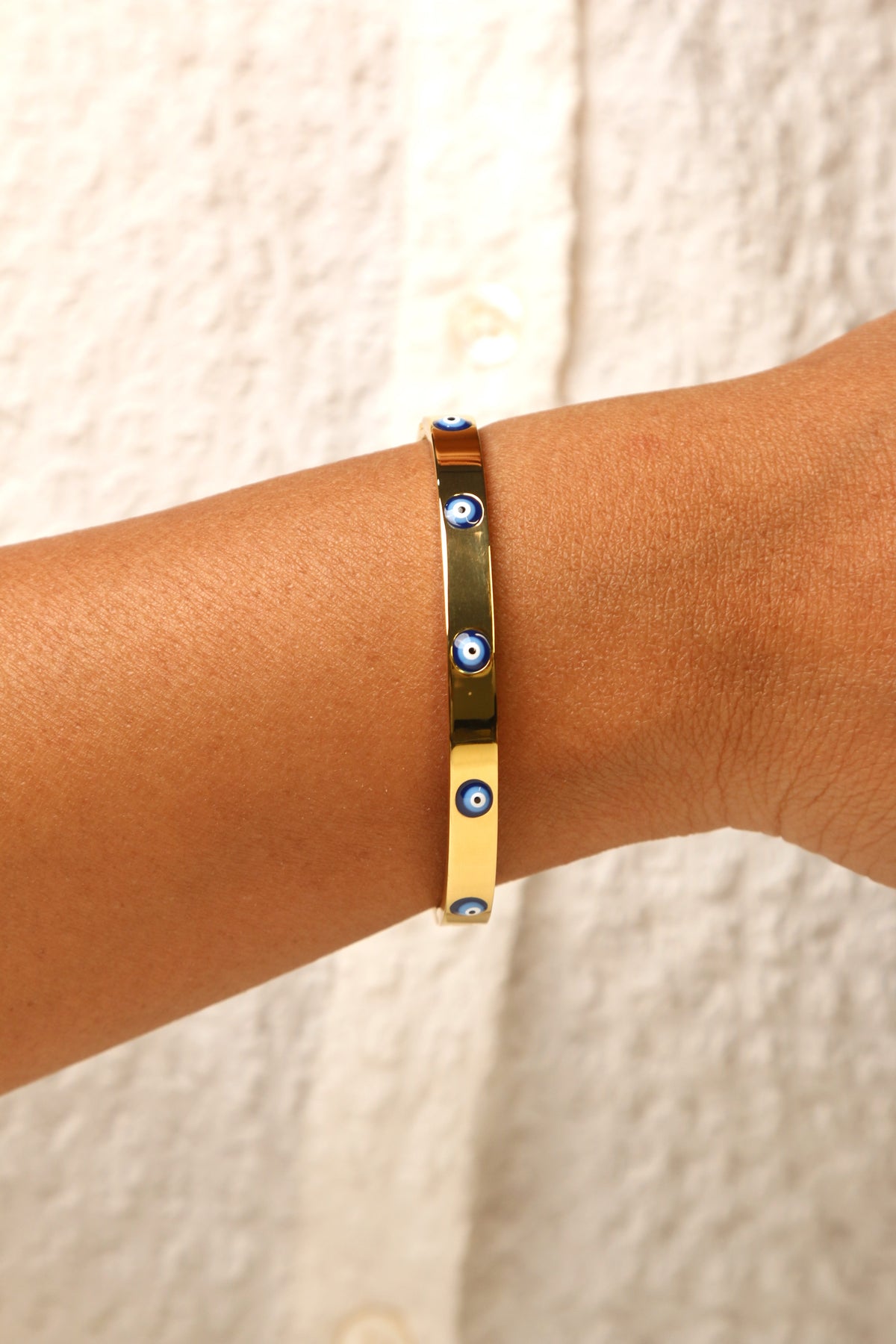 Gold-tone evil eye bracelet with a modern glow effect.