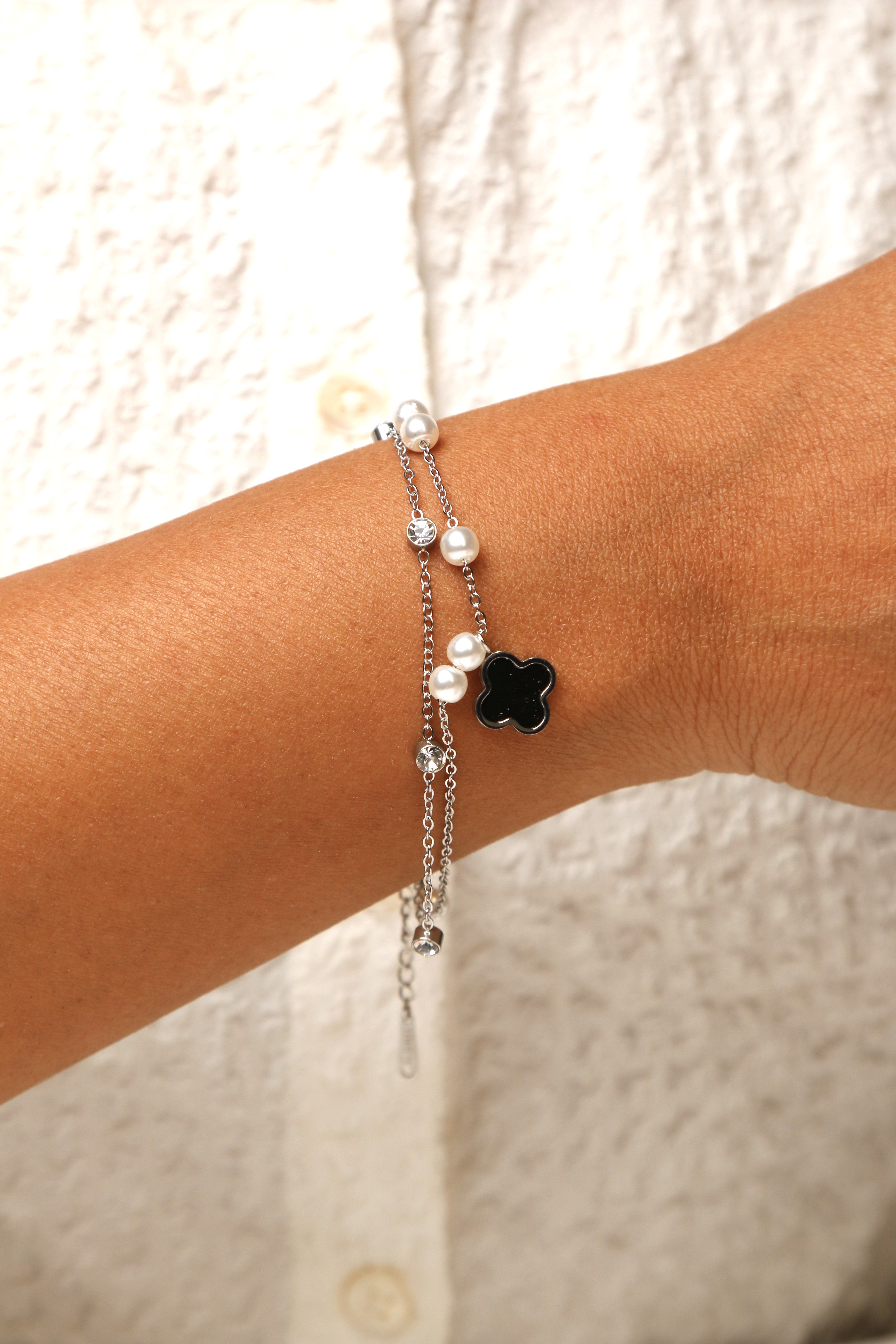 Black clover charm bracelet with layered pearl design.