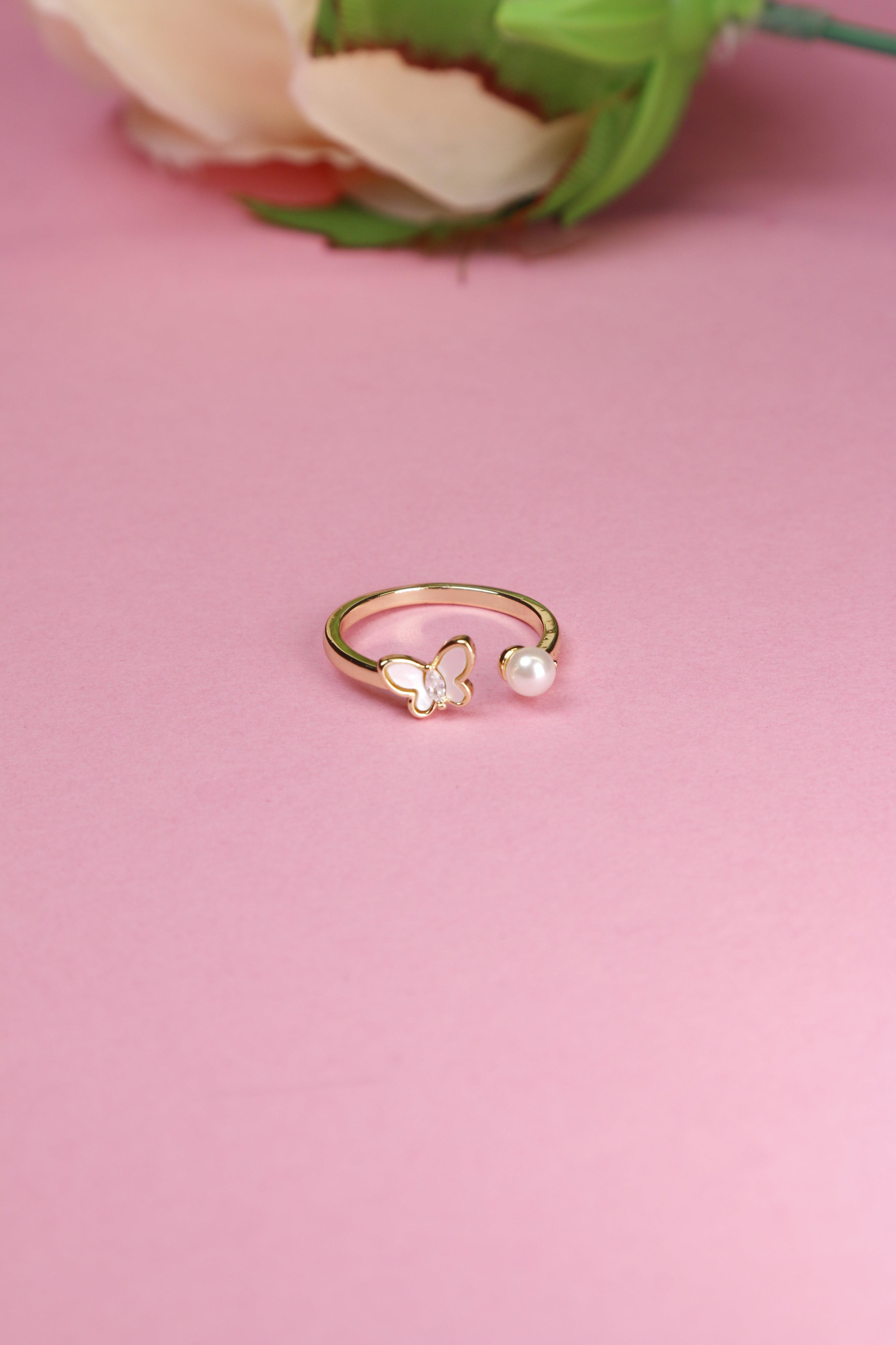 Butterfly ring with a pearl on one side, set on a pink background.