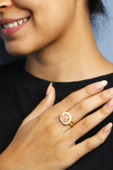 Close-up shot of a woman's hand wearing a floral gold ring with a pink flower, emphasizing the beauty of the delicate design.