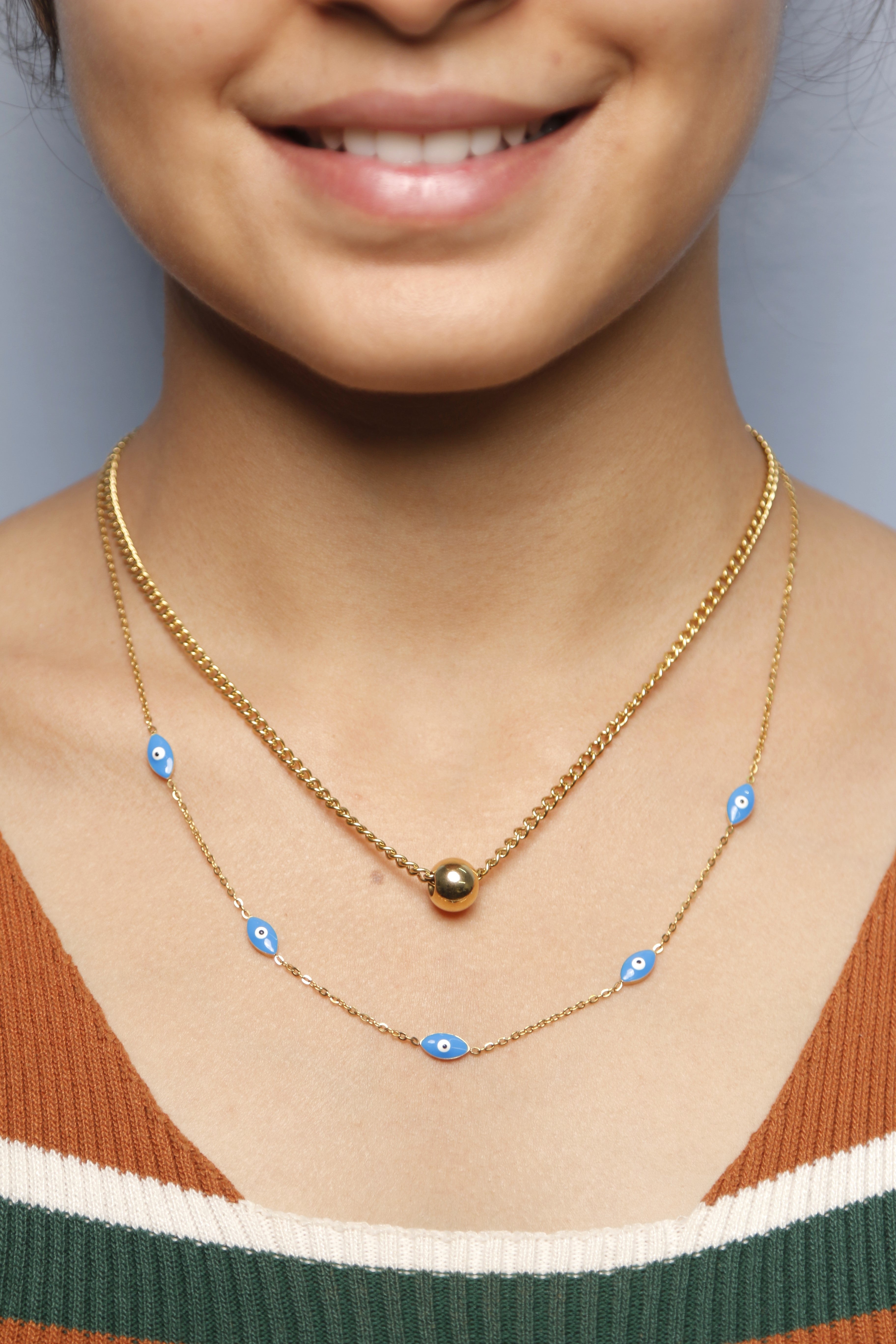A woman wearing a gold ball and blue eye pendant necklace.