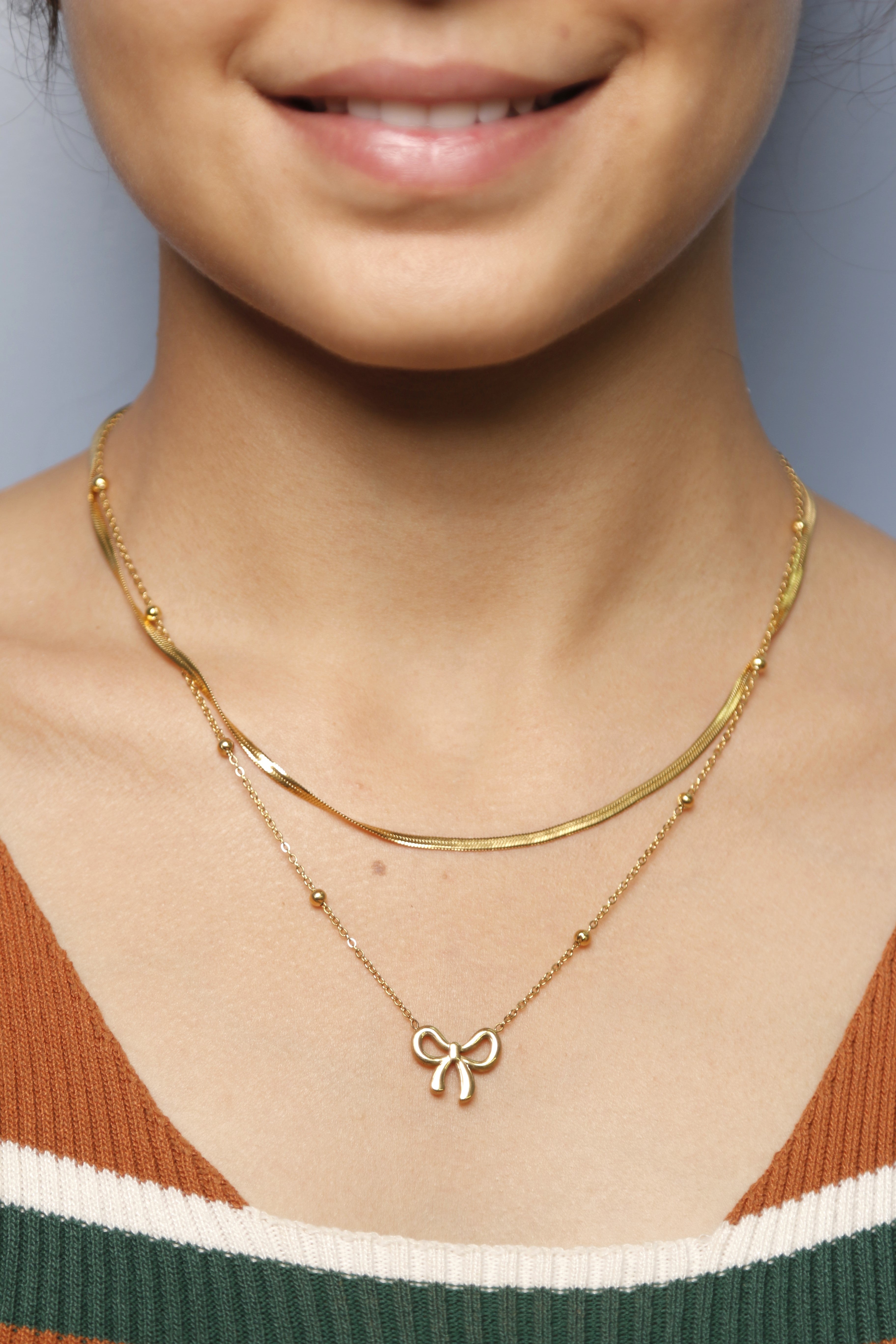 Close-up image of a woman wearing a gold bow necklace.