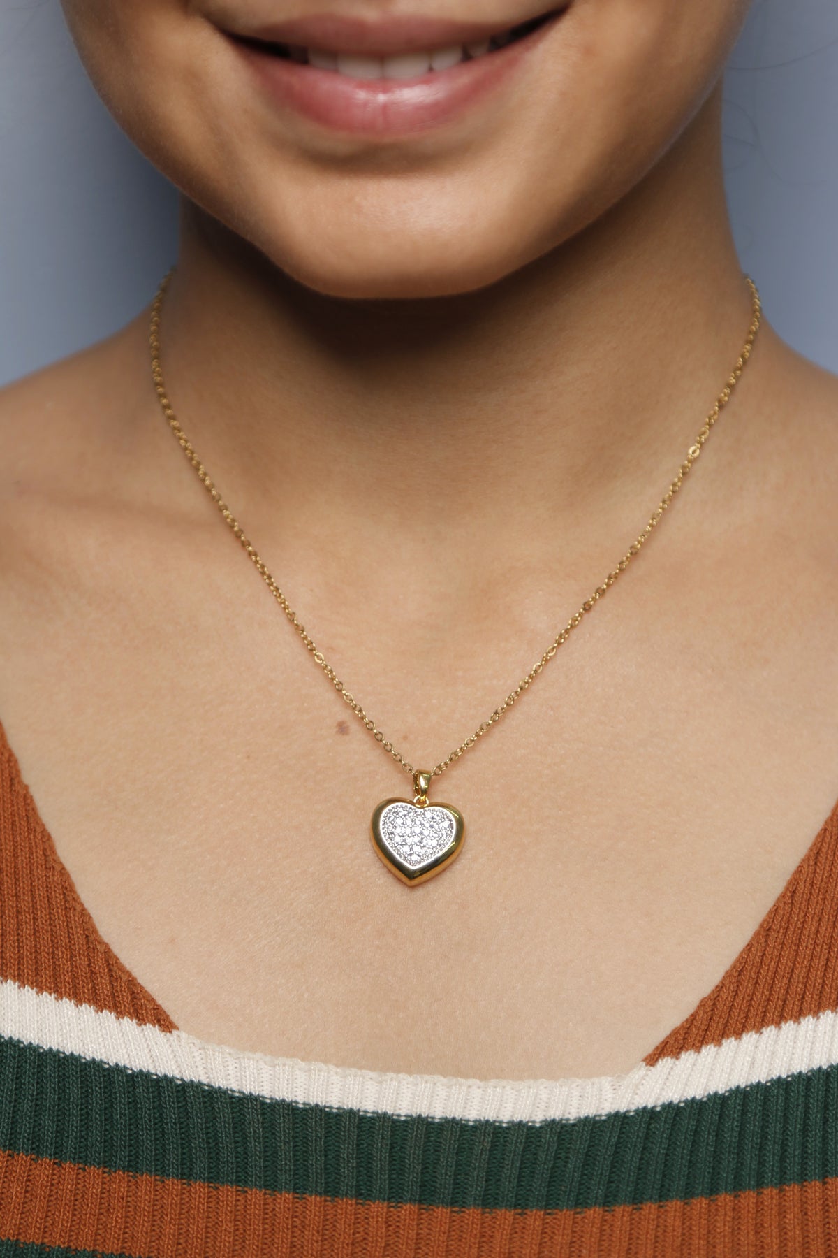 A woman gently touching her gold heart-shaped necklace with diamonds.
