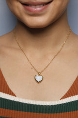 A woman gently touching her gold heart-shaped necklace with diamonds.