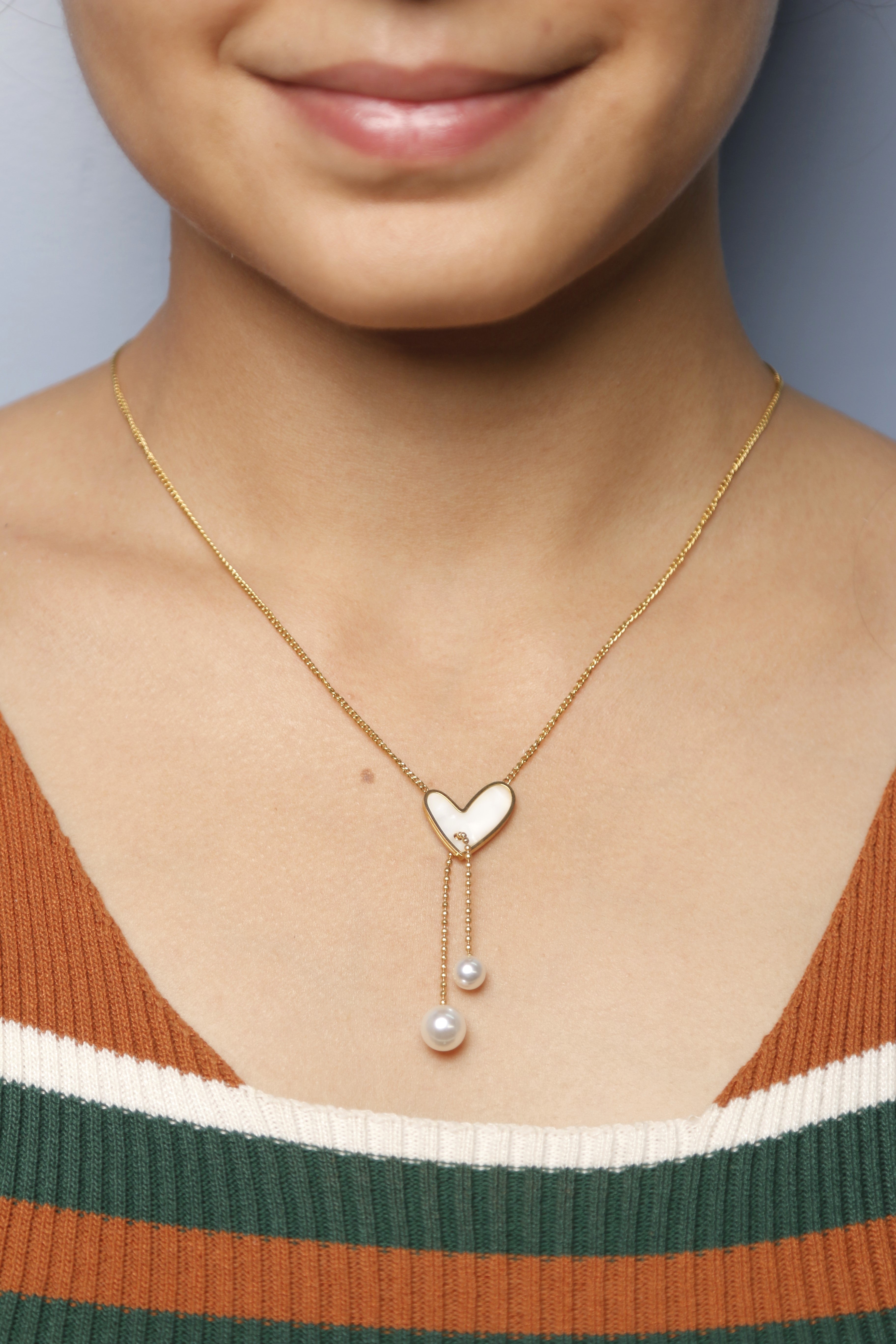 Close-up of a woman wearing a gold heart-shaped necklace with two dangling pearl drops