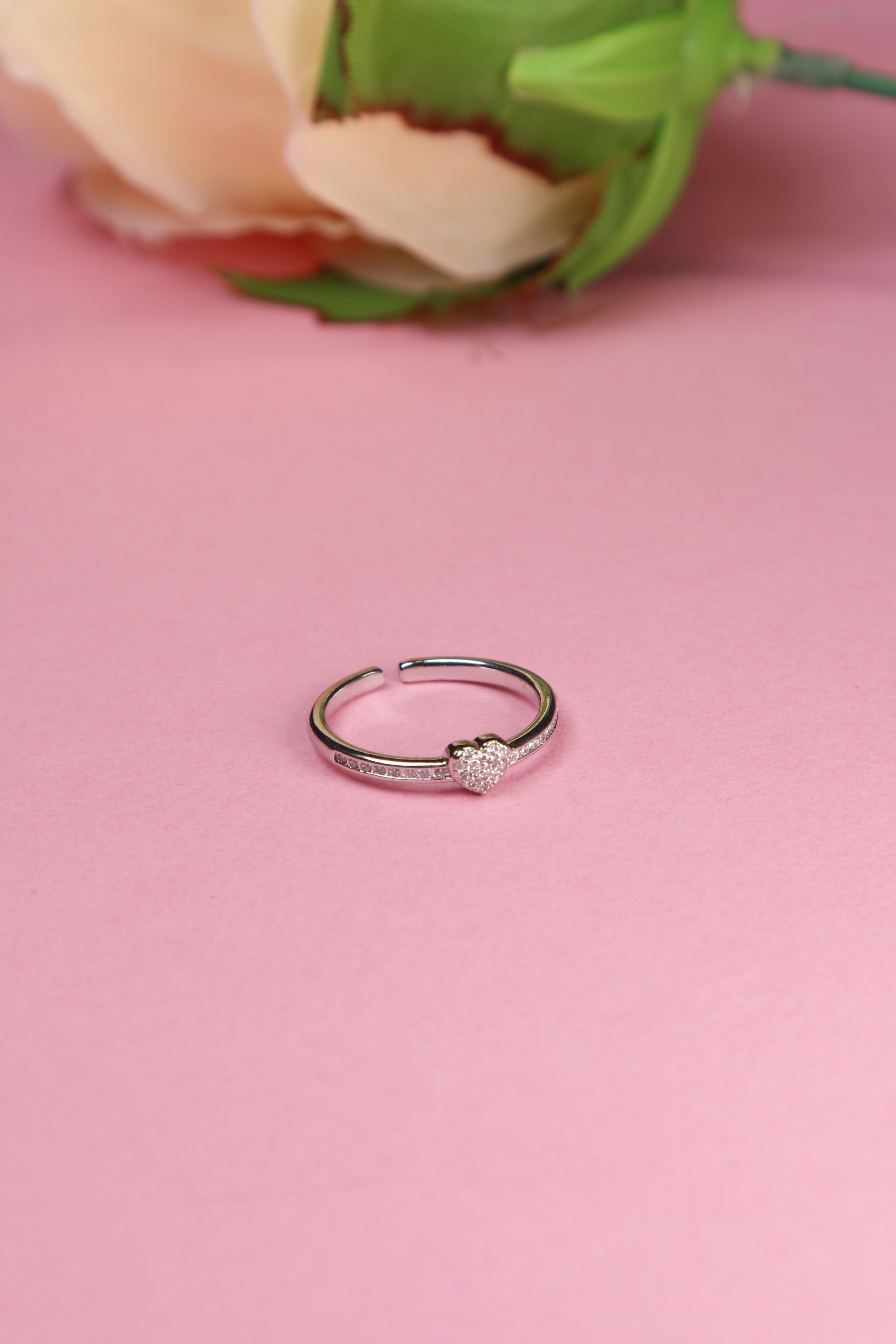 Heart ring with diamond detailing, placed on a pink background.