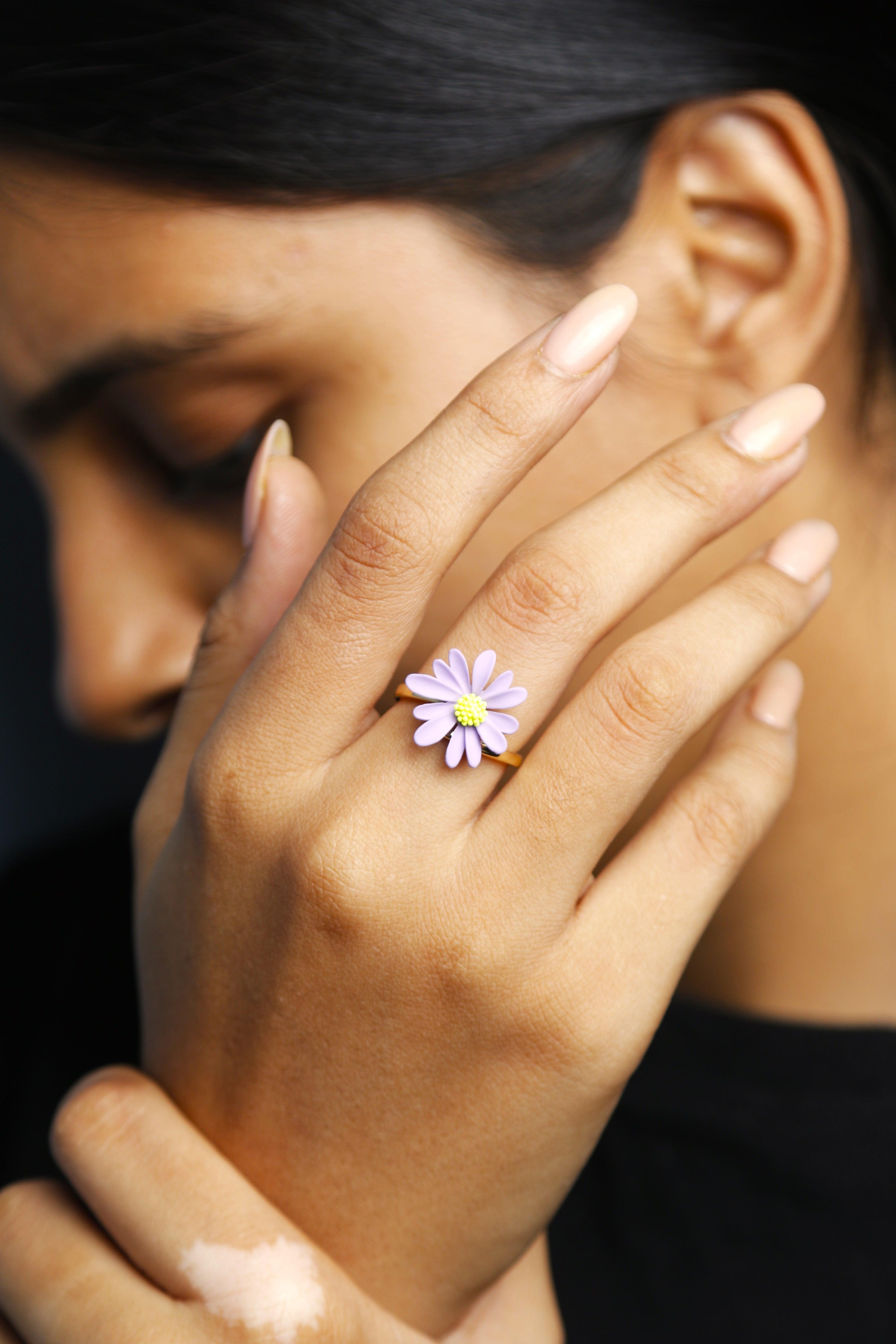 A close-up view of a purple daisy flower ring with soft petals and a yellow center, set on a simple gold band.
