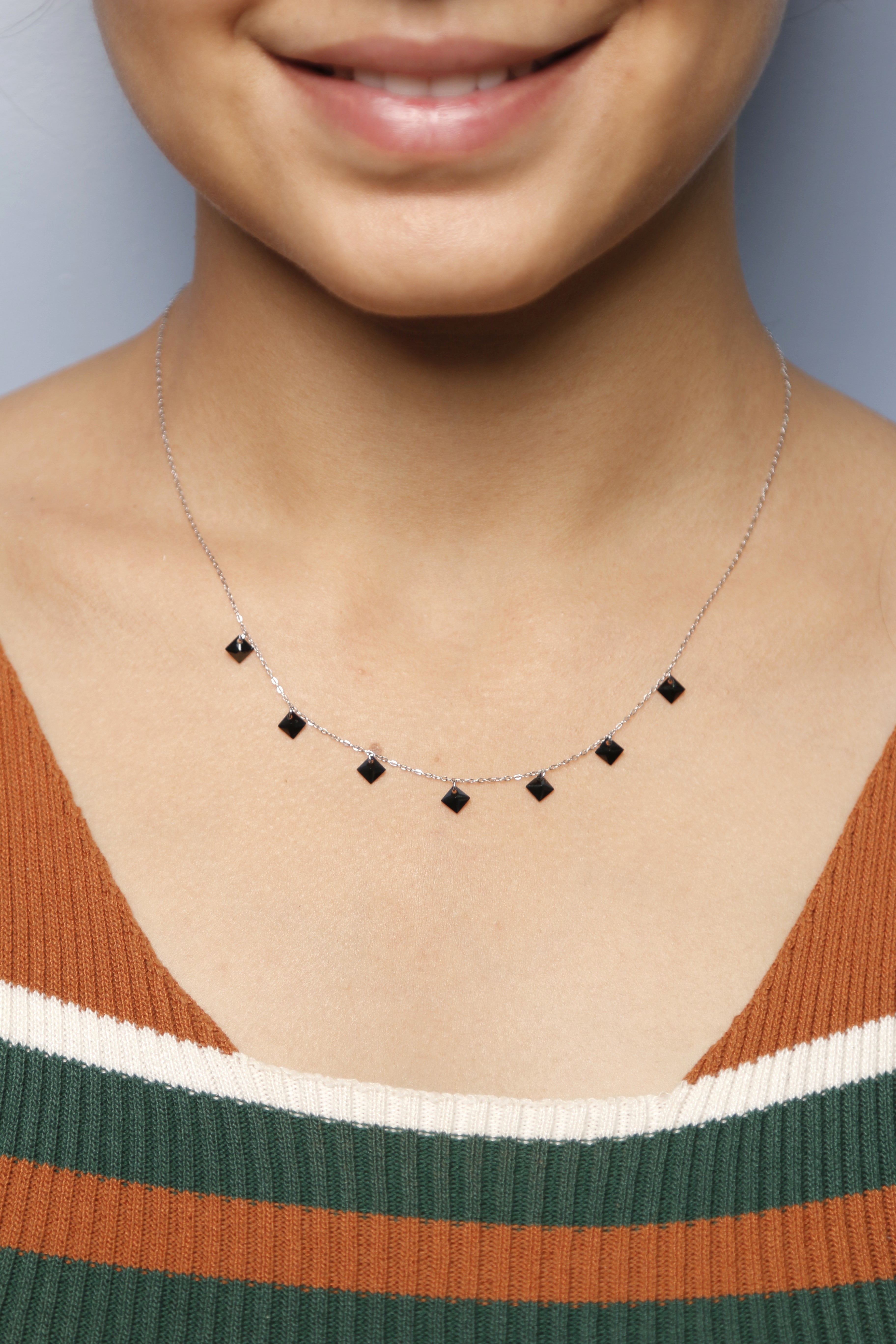 A close-up of a woman wearing a silver necklace with black square stones.
