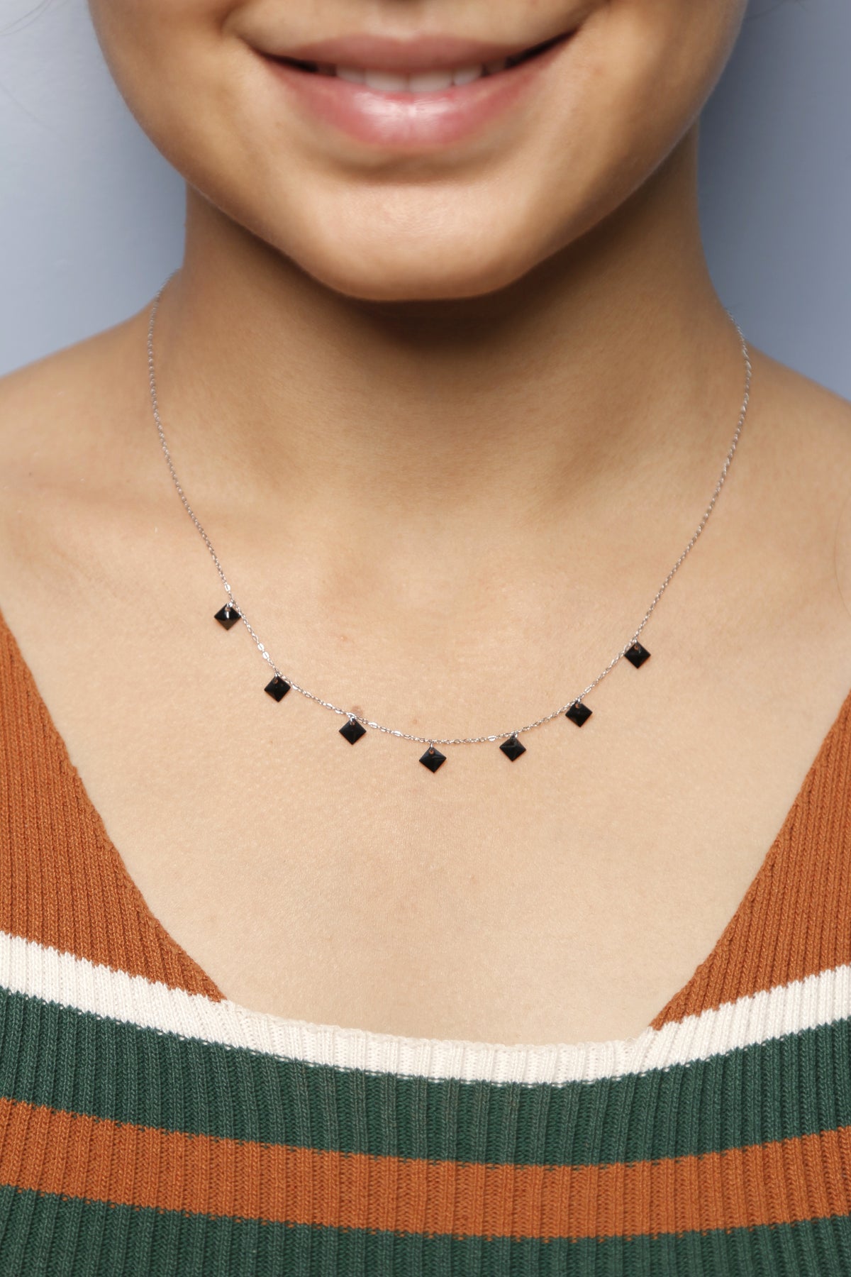A close-up of a woman wearing a silver necklace with black square stones.
