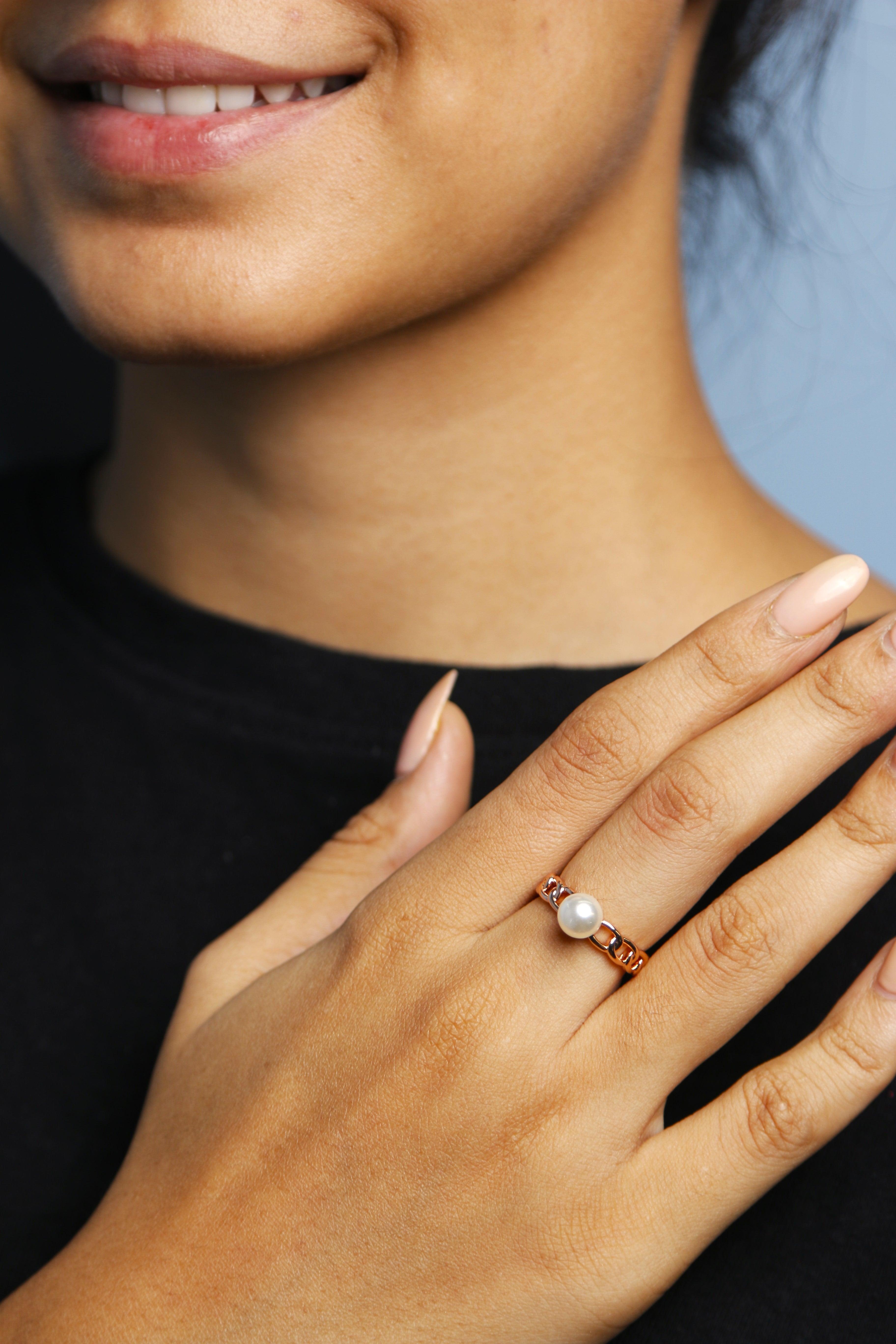 A woman is wearing a stunning rose gold chain pearl ring on her finger, smiling gently.