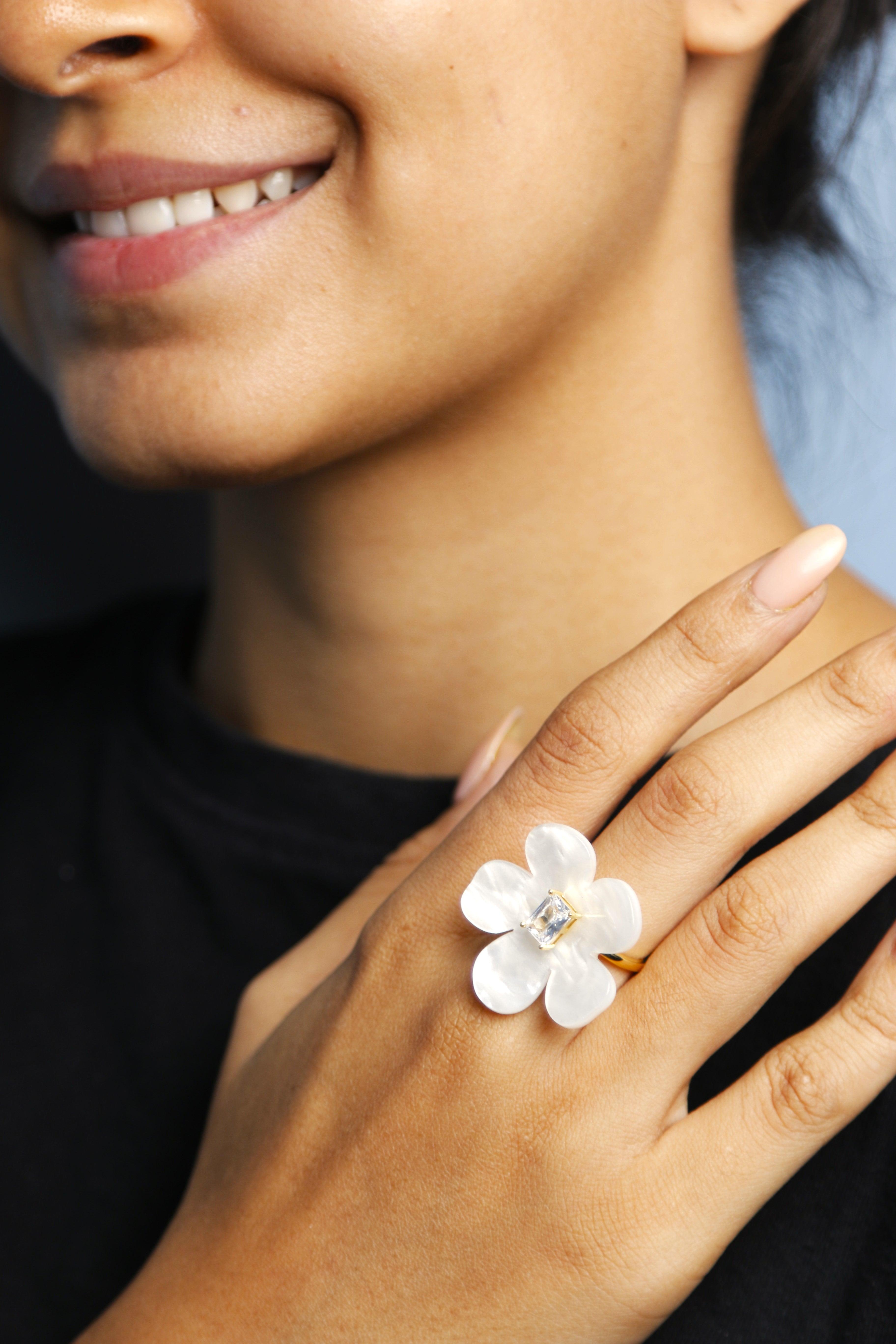 Woman wearing a floral white ring with a center gemstone, adding a touch of elegance.