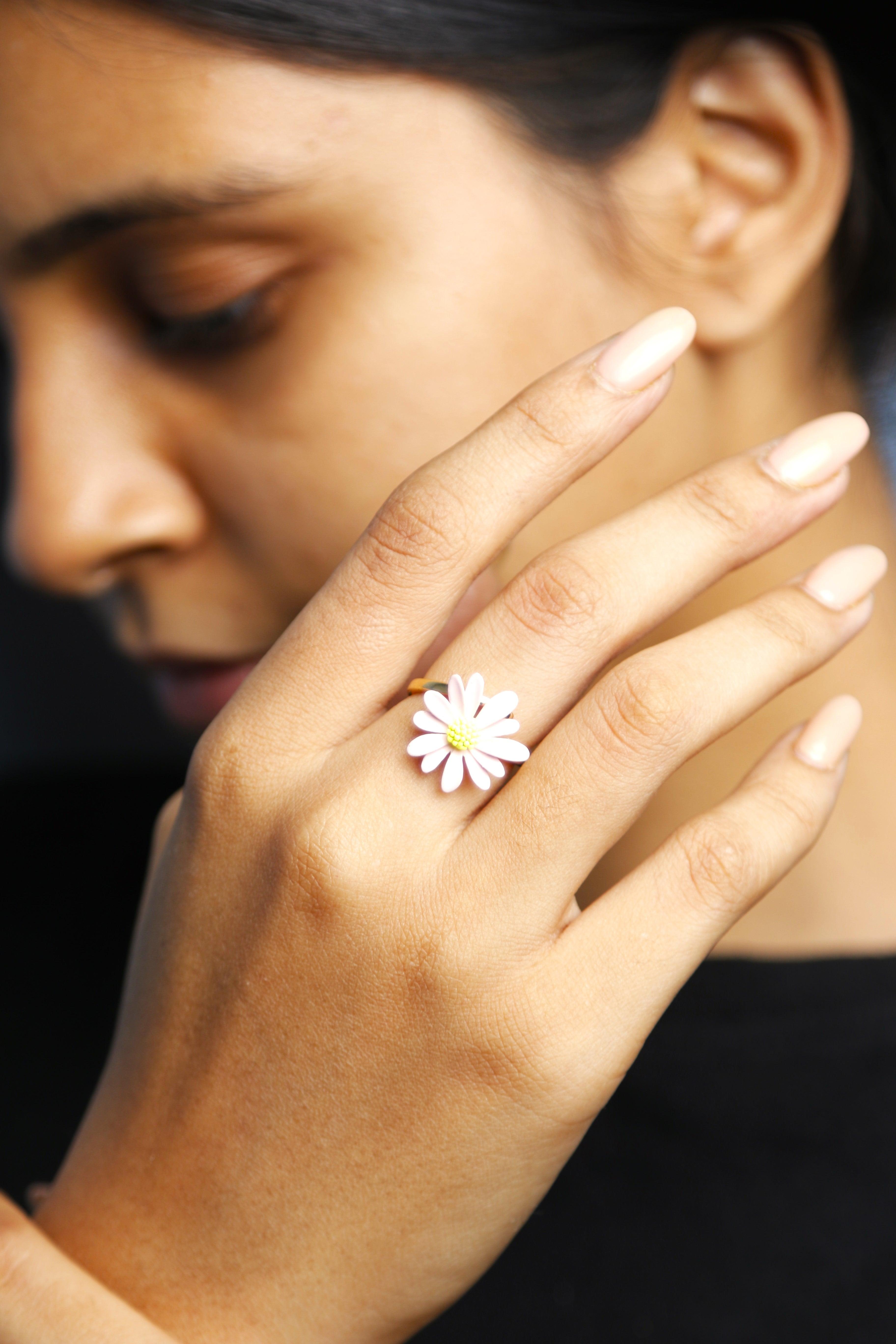 A young woman gently holding her hand with a flower ring. The focus is on the ring's design