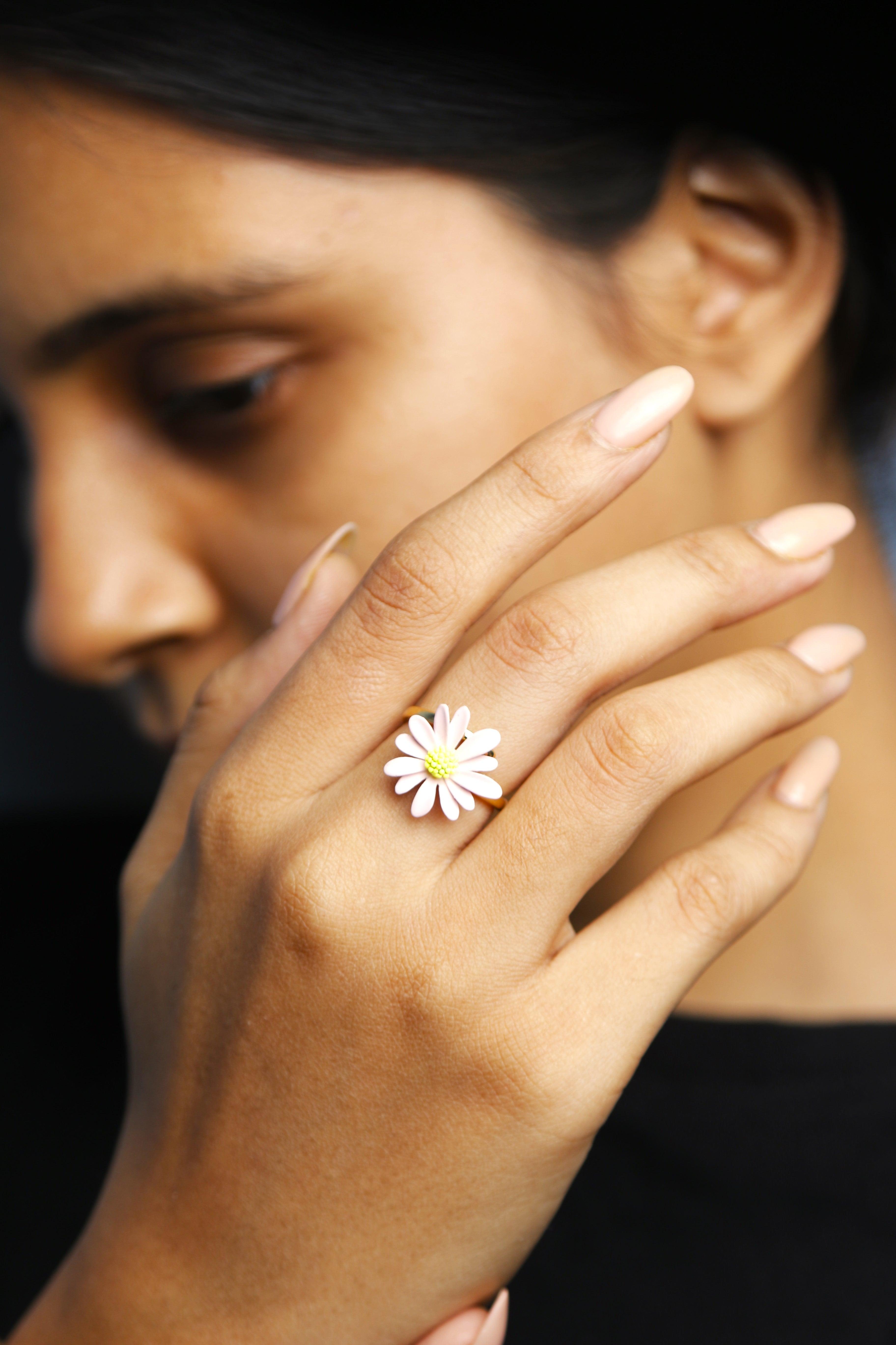 A young woman showcasing her flower ring. The ring features yellow center, displayed with a subtle background to highlight the jewelry.