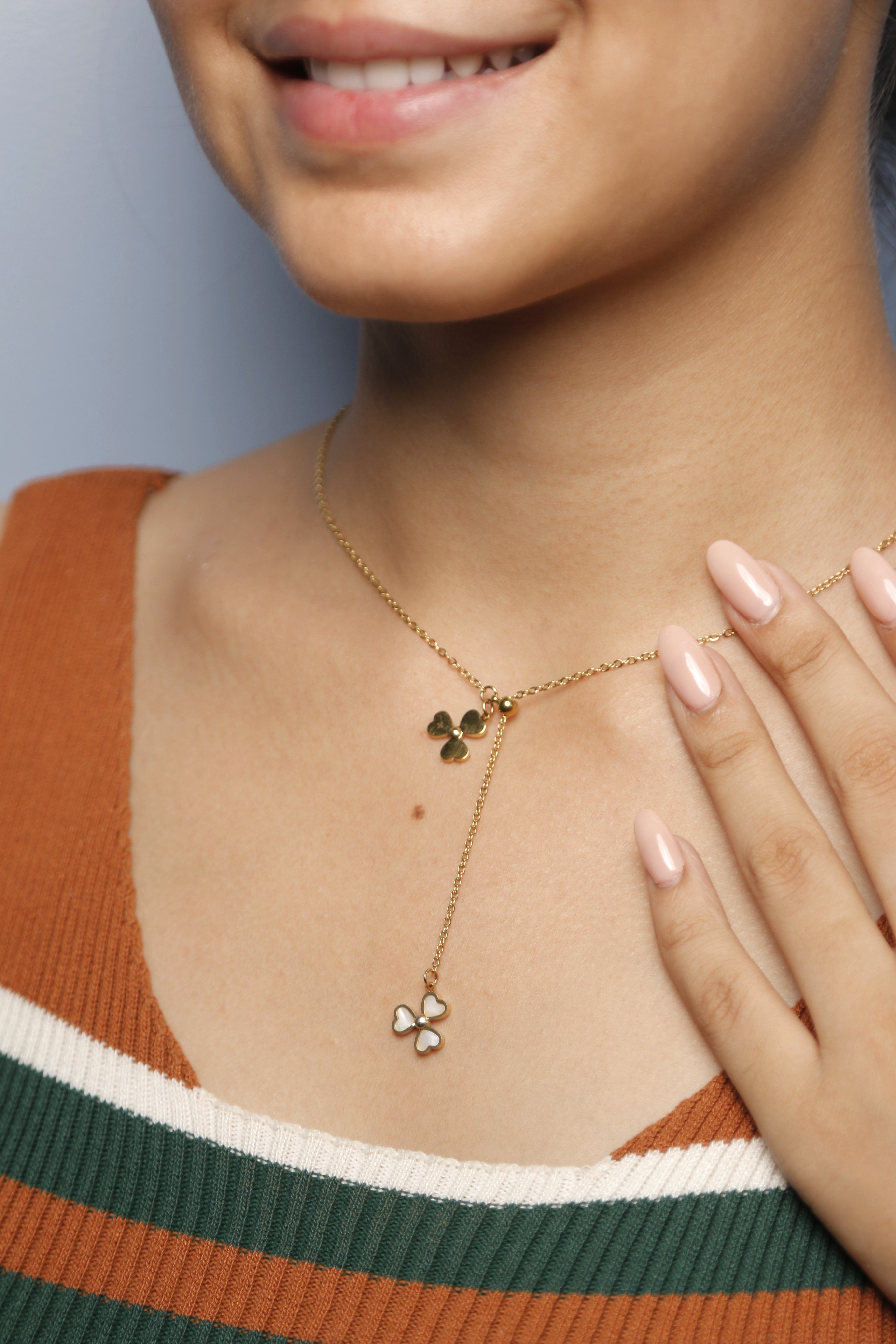 A woman adjusting her gold Flower heart-shaped necklace.