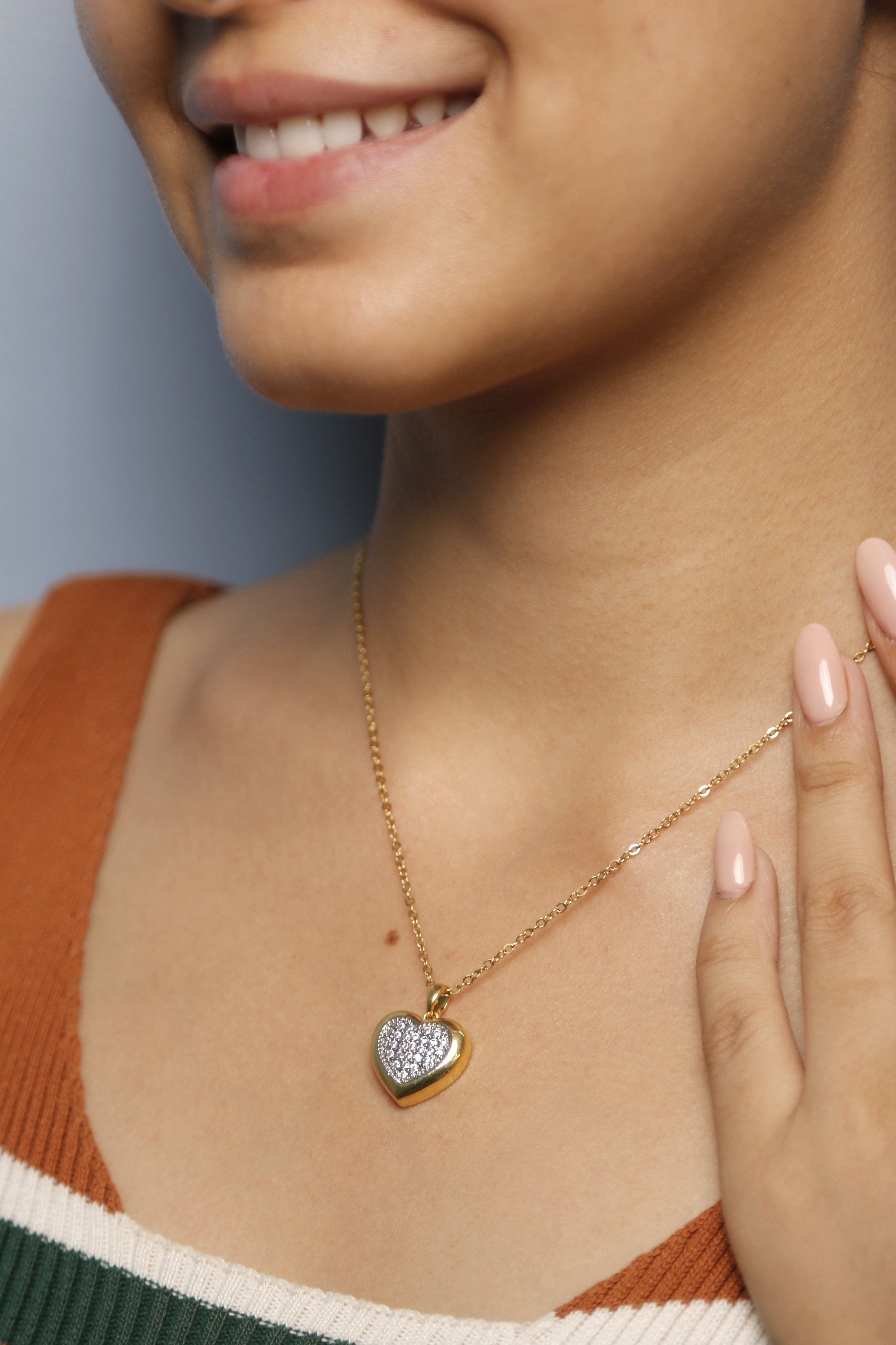 A woman gently touching her gold heart-shaped necklace with diamonds.