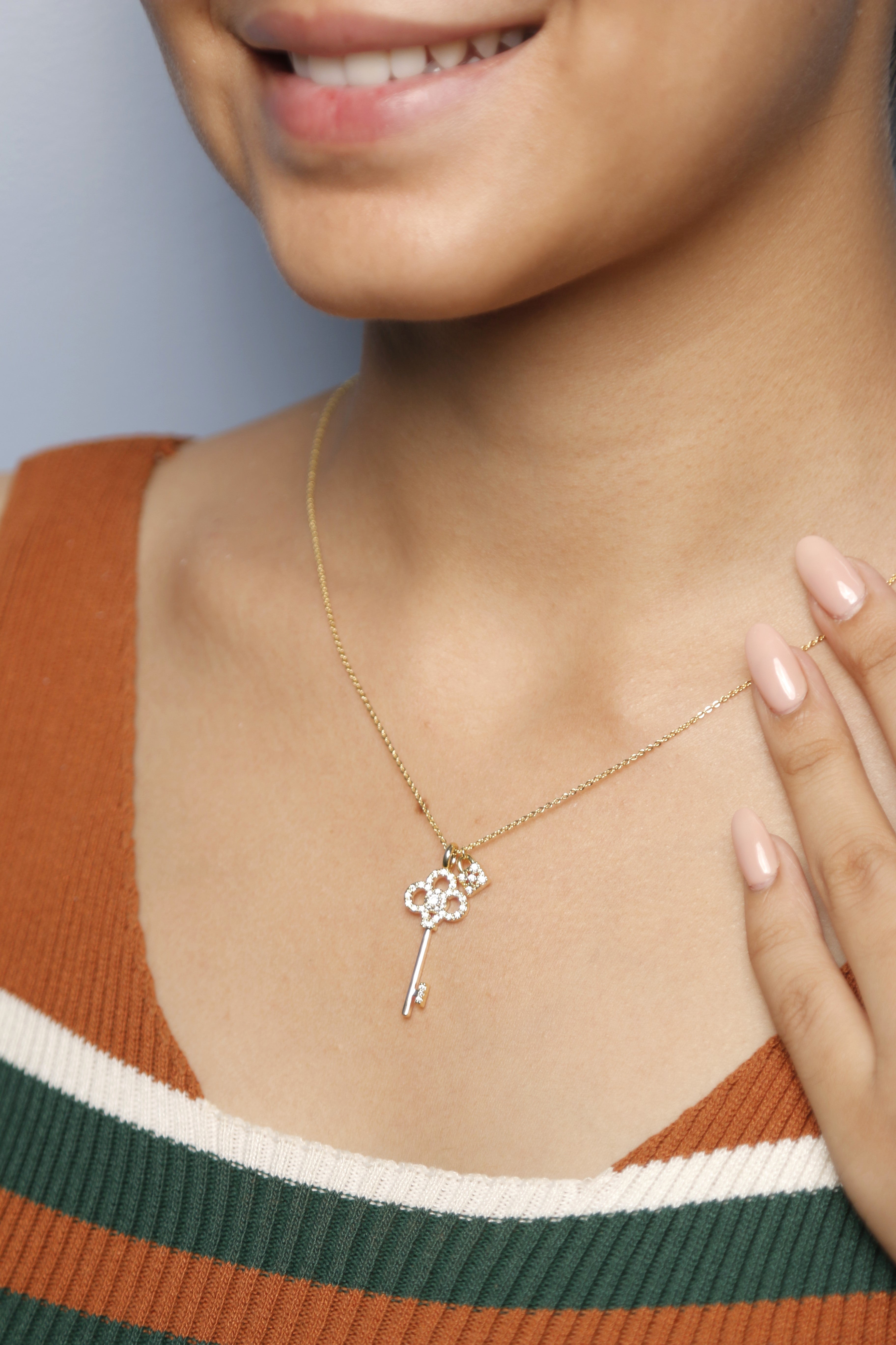 A woman gently adjusting her gold key-shaped necklace, embellished with diamonds.