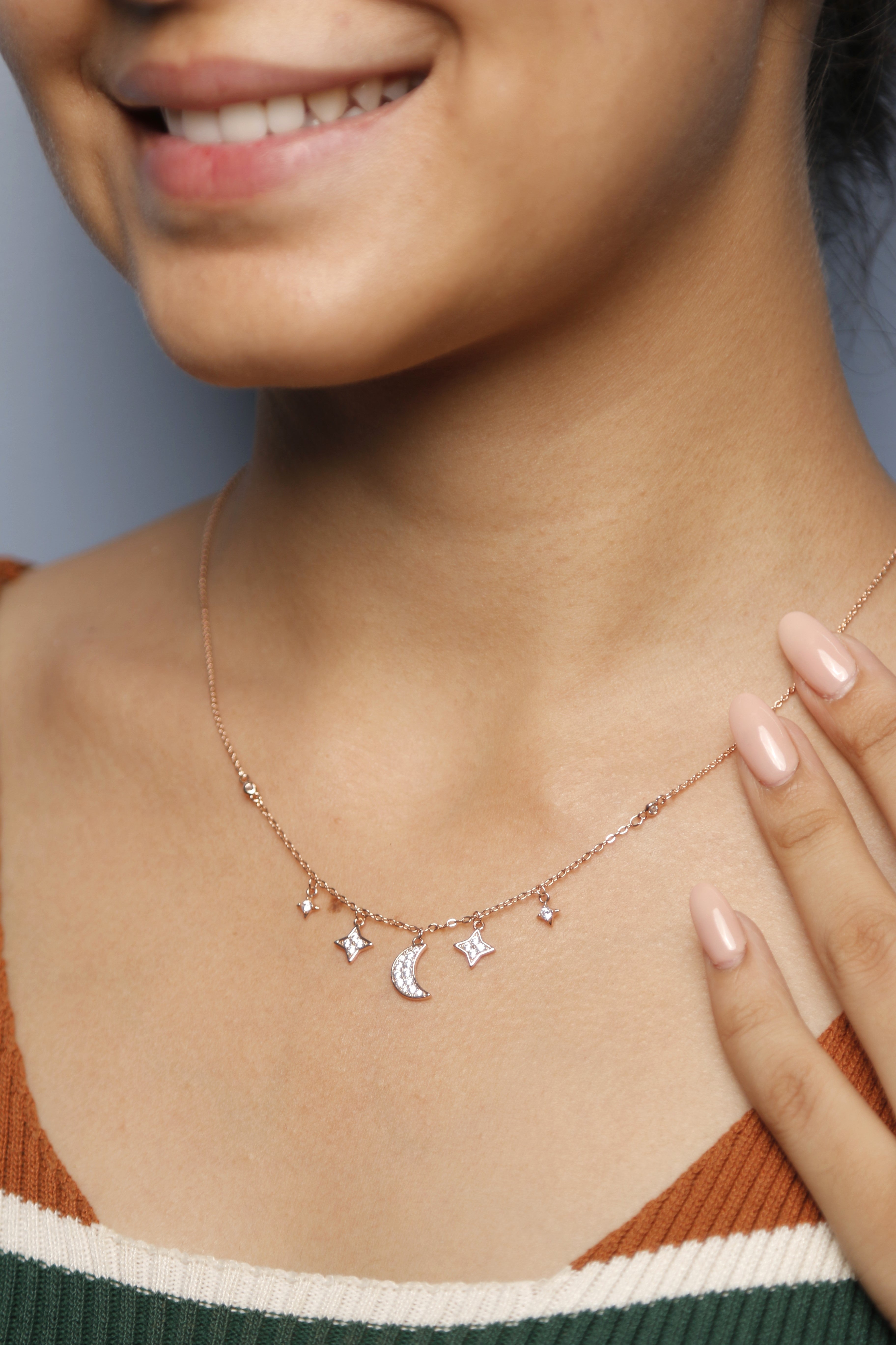 A woman gently touching her rose gold necklace adorned with moon and star pendants.