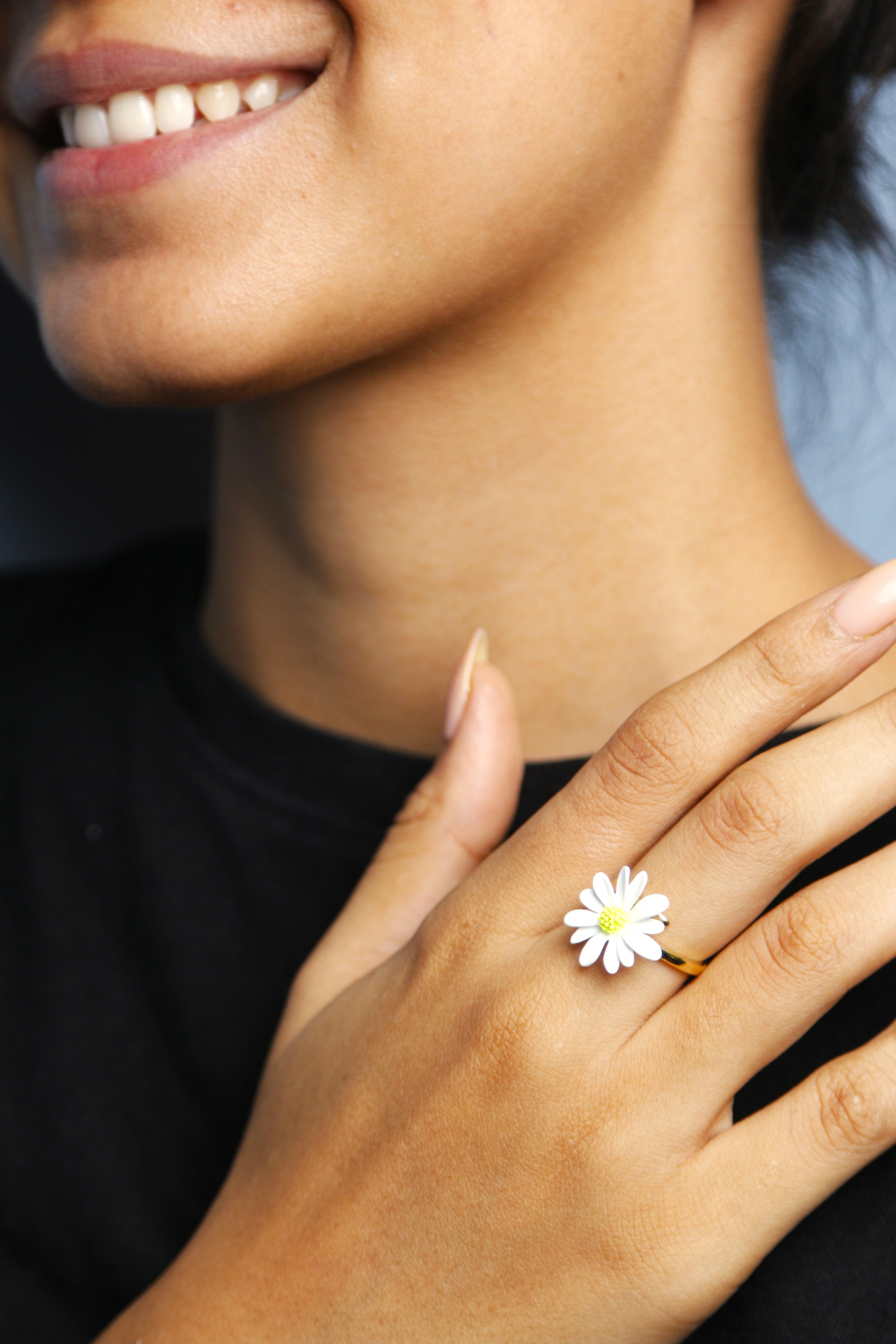 A young woman wearing a flower ring, showcasing it on her hand with a soft background.