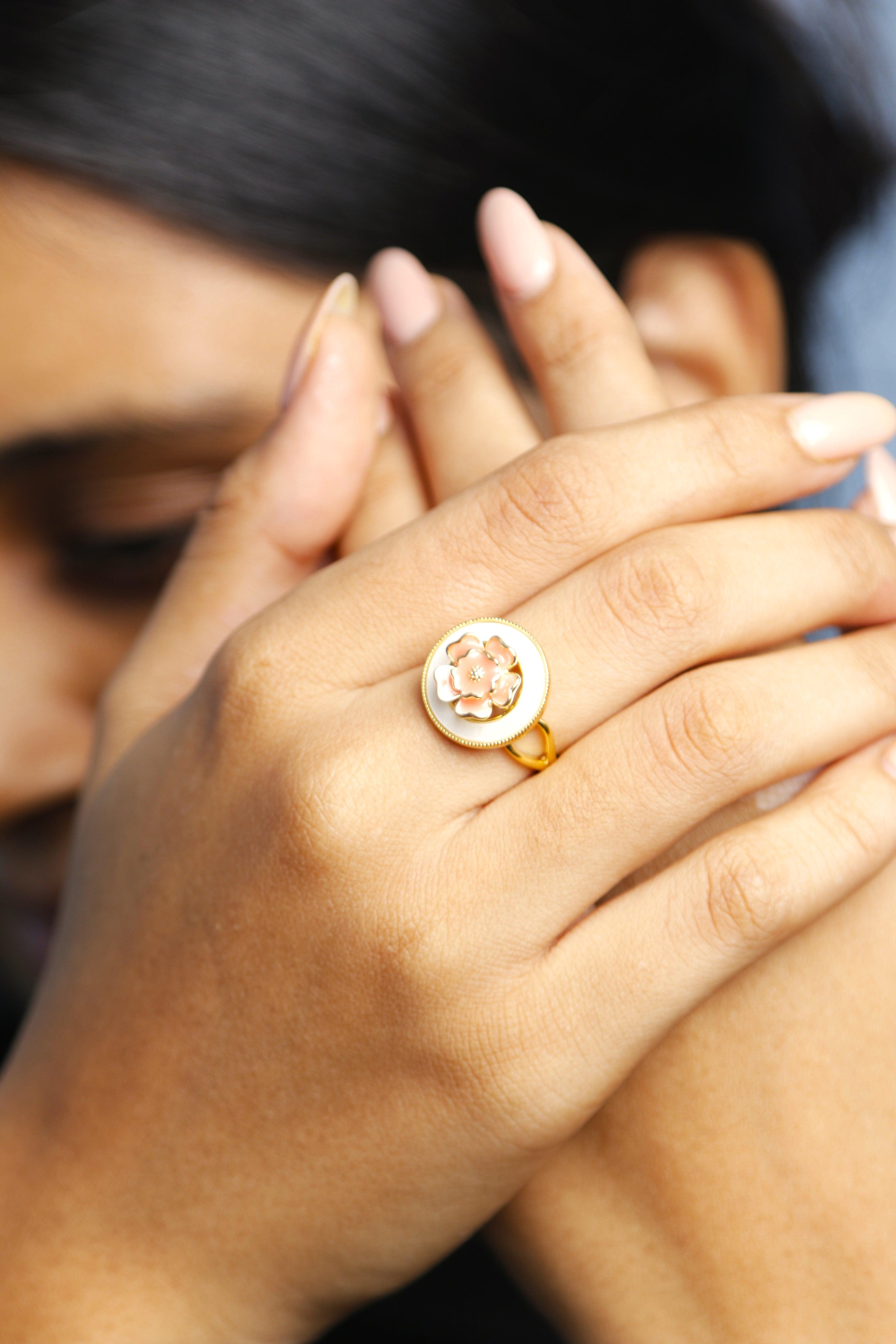 A woman wearing a beautiful gold ring with a pink floral design on her finger, showcasing the delicate craftsmanship of the jewelry.